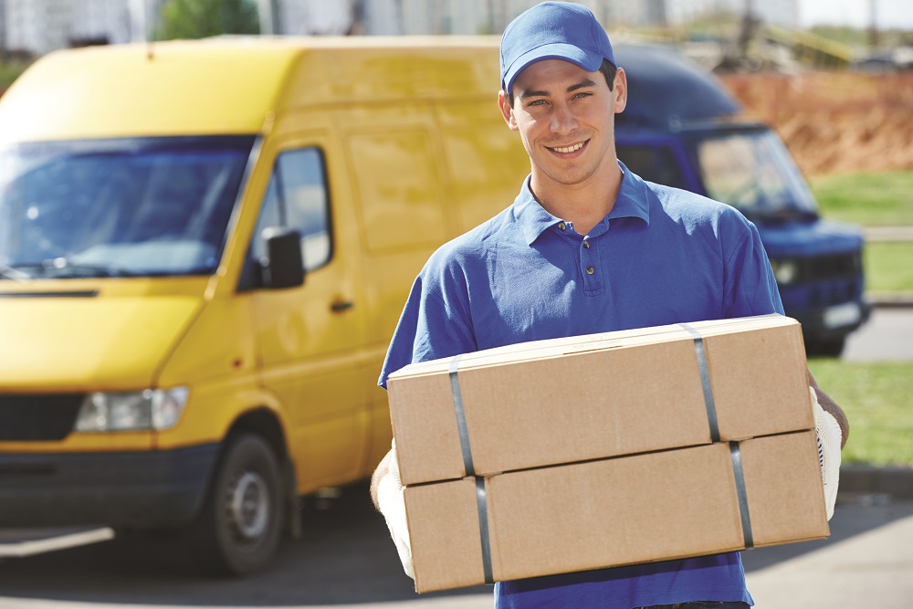 Smiling young male postal delivery courier man in front of cargo van delivering package